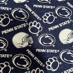 Peut inclure: Tissu bleu marine avec un motif répété de logos blancs de l'Université Penn State, de casques de football et d'empreintes de pattes. Les mots "PENN STATE" sont également imprimés. Le tissu a une texture mouchetée.