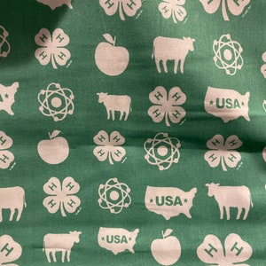 May include: Green fabric with a repeating pattern of white 4-H clover emblems, apples, cows, atom symbols, and USA map outlines. The fabric has a slightly wrinkled texture.