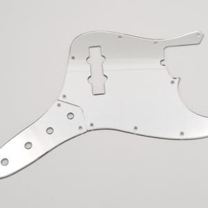 Puede incluir: Un golpeador de bajo de color plateado con un gran recorte para la pastilla y varios agujeros más pequeños para los tornillos.