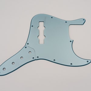 May include: A light blue bass guitar pickguard with a cutout for the pickup and control knobs.