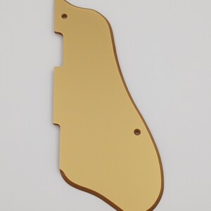 May include: Gold-colored guitar pickguard with rounded edges and two small holes.