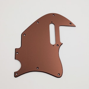 May include: A copper-colored guitar pickguard with a cutout for a single-coil pickup and a control plate. The pickguard has a smooth, metallic finish.