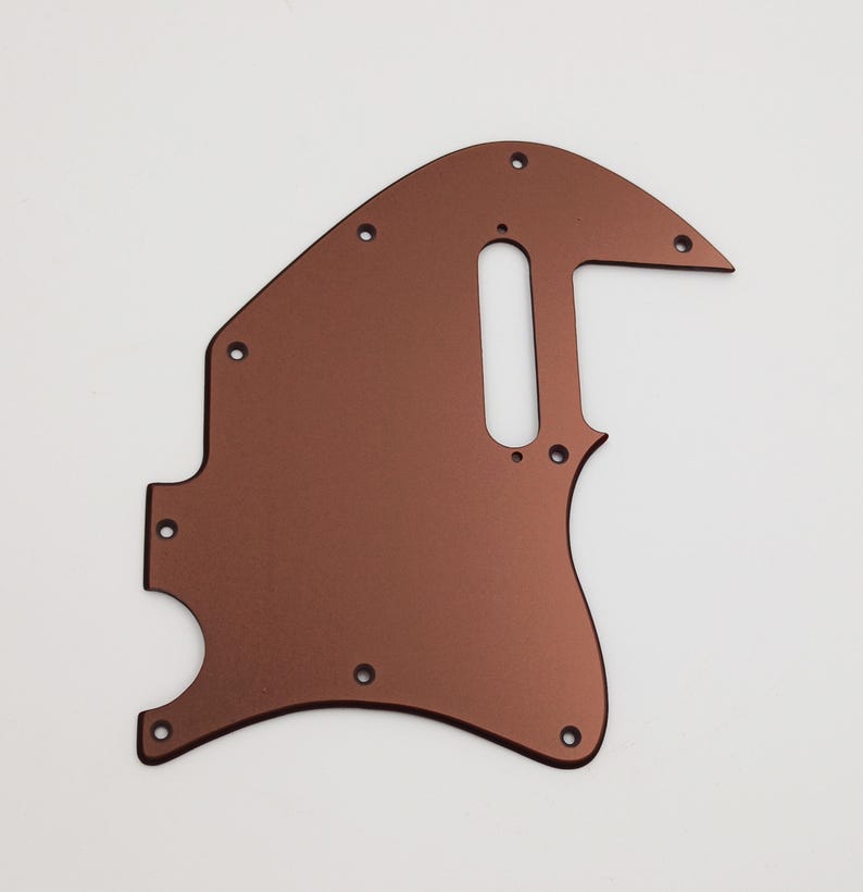 May include: A copper-colored guitar pickguard with a cutout for a single-coil pickup and a control plate. The pickguard has a smooth, metallic finish.
