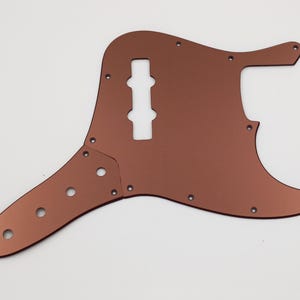 May include: A copper-colored bass guitar pickguard with multiple screw holes and a large cutout for the pickup.