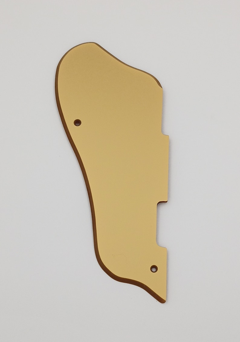 May include: Gold-colored guitar pickguard with a rounded shape and two small holes.