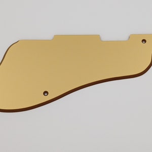 May include: Gold-colored guitar pickguard with rounded edges and three small holes.
