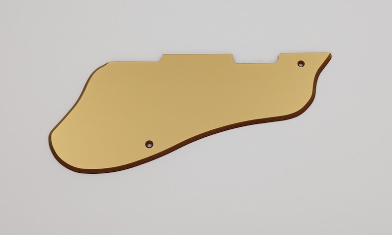 May include: Gold-colored guitar pickguard with rounded edges and three small holes.