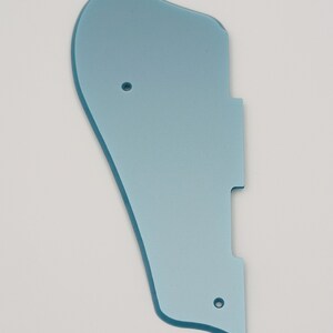 May include: A light blue plastic guitar pickguard with three holes.