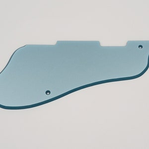 May include: A light blue guitar pickguard with a unique shape, featuring two screw holes and a contoured edge. The pickguard is made of a solid, opaque material and is designed to protect the guitar's body.