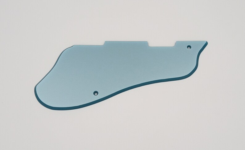 May include: A light blue guitar pickguard with a unique shape, featuring two screw holes and a contoured edge. The pickguard is made of a solid, opaque material and is designed to protect the guitar's body.