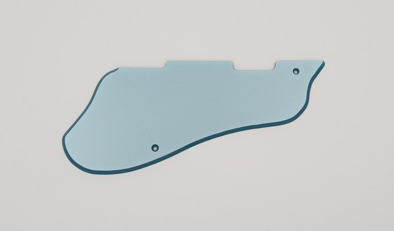 May include: A light blue guitar pickguard with a curved, asymmetrical shape. The pickguard has two small holes for mounting and a dark blue outline. The object is set against a white background.