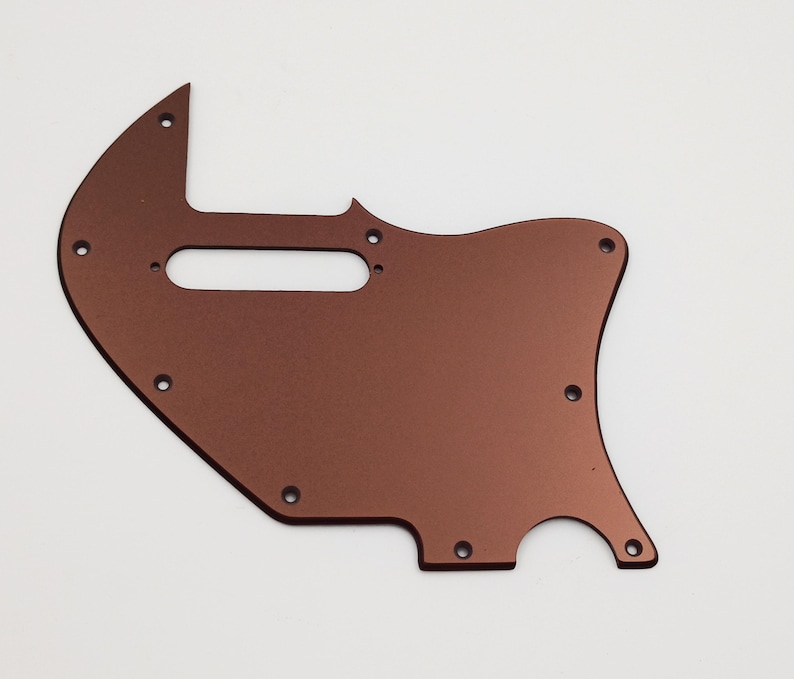 May include: A copper-colored guitar pickguard with multiple screw holes and a cutout for a pickup.