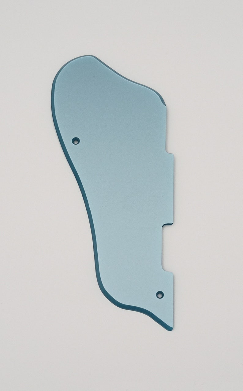 May include: A light blue guitar pickguard with a unique shape, featuring two screw holes and a cutout. The pickguard has a smooth surface and is designed to protect the guitar's body from scratches. It is a replacement part for an electric guitar.