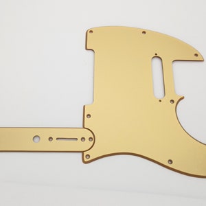 Peut inclure: Un pickguard de guitare de couleur or avec une plaque de contrôle. Le pickguard est en forme de corps de guitare et comporte plusieurs trous pour les vis et les boutons. La plaque de contrôle est une longue pièce rectangulaire avec des trous pour les boutons et un interrupteur.