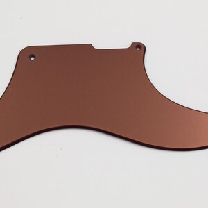 Peut inclure: Un pickguard de guitare de couleur cuivre avec des bords arrondis et quatre trous de vis.