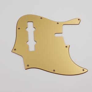 Könnte beinhalten: Goldfarbener Gitarren-Pickguard mit einer Aussparung für einen Tonabnehmer und Reglerknöpfe.