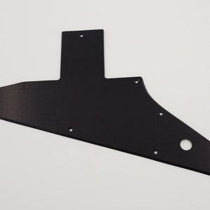 Peut inclure: Un pickguard de guitare noir avec plusieurs trous de vis et un seul grand trou.