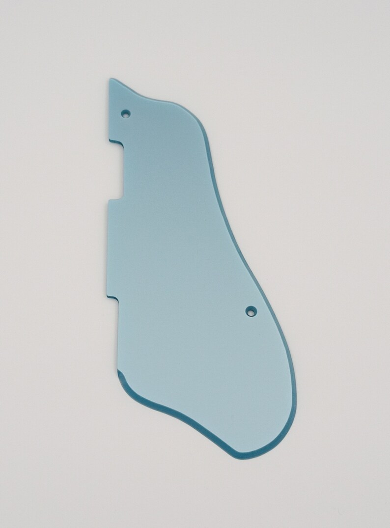 May include: A light blue guitar pickguard with a unique shape, featuring two pre-drilled holes for mounting. The pickguard has a smooth, glossy finish and is designed to protect the guitar's body from scratches.