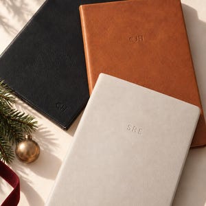 May include: Three rectangular notebooks with textured covers in black, tan, and light gray. The black notebook is embossed with the letters CH, the tan notebook with CJH, and the light gray notebook with SRE. Each notebook has a smooth, solid-colored finish.