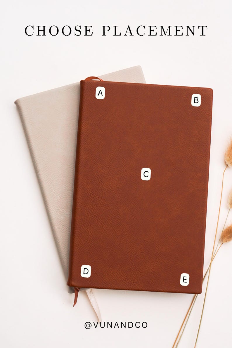 May include: Two leather-bound journals, one tan and one brown, are displayed on a white surface. The brown journal is open, revealing a tan interior. The text "CHOOSE PLACEMENT" is at the top, and the brand name is at the bottom.
