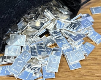May include: A collection of small, rectangular 1 gram silver bars spilling out of a black velvet pouch. Each metallic bar features the Valcambi logo, the text 1g, fine silver, and 999.0, with a square emblem embossed on the reflective surface.
