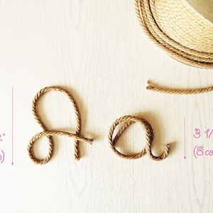 May include: A brown jute rope shaped into the letters A and a, accompanied by a spool of the same rope. The letter A measures 6 1/4 inches in height, while the letter a measures 3 1/8 inches in height, as indicated by pink text labels.