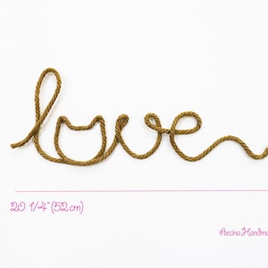Puede incluir: Una cuerda marr&oacute;n est&aacute; formada en la palabra "love" con un coraz&oacute;n en la "o". La cuerda tiene 18 cm de alto y 52 cm de ancho.