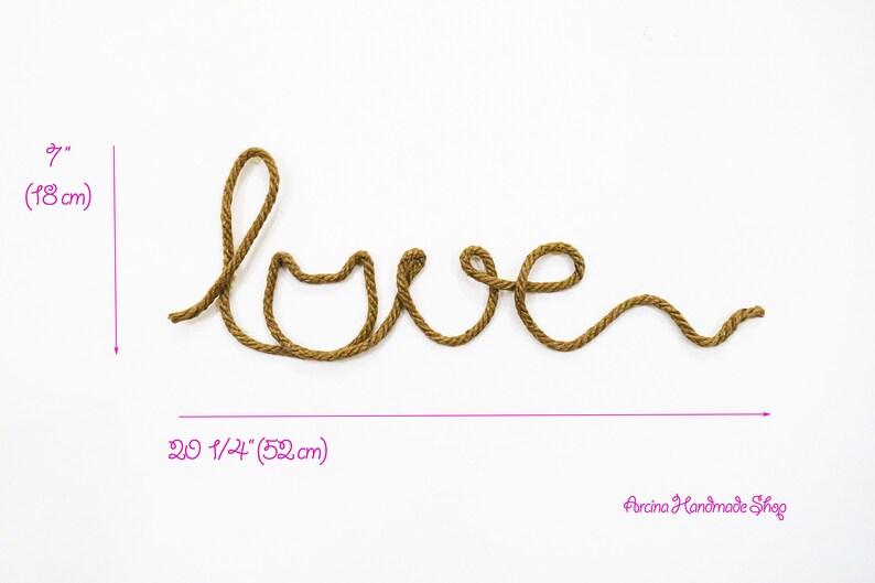 Puede incluir: Una cuerda marr&oacute;n est&aacute; formada en la palabra "love" con un coraz&oacute;n en la "o". La cuerda tiene 18 cm de alto y 52 cm de ancho.