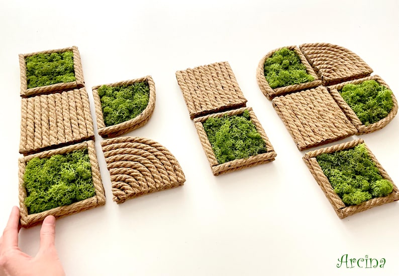 May include: A collection of modular wall tiles featuring natural green moss encased in frames made of coiled tan rope. The set includes square and quarter-circle shapes with textured rope surfaces and vibrant green preserved moss inserts.