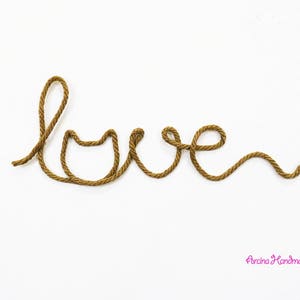 Puede incluir: La palabra "love" deletreada con hilo marr&oacute;n sobre un fondo blanco. La palabra "love" est&aacute; escrita en cursiva. El hilo es de color natural y tiene una textura rugosa. El fondo es una superficie blanca lisa.