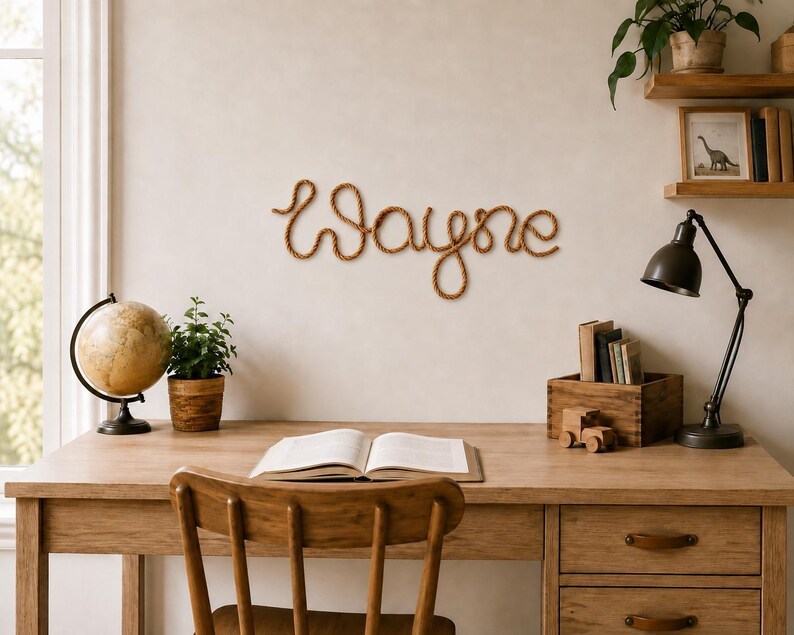 May include: A wall-mounted sign featuring the name Wayne written in a continuous, cursive script made from a thick, brown, twisted rope material. The letters are connected in a single flowing line, creating a decorative piece of wall art.