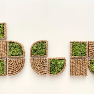 May include: A collection of modular wall art pieces featuring natural green moss encased in frames wrapped with tan jute rope. The set includes square and semi-circular shapes with textured rope patterns and organic moss textures. The word Arcina is visible.