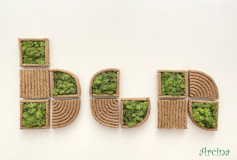 May include: A collection of modular wall art pieces featuring natural green moss encased in frames wrapped with tan jute rope. The set includes square and semi-circular shapes with textured rope patterns and organic moss textures. The word Arcina is visible.