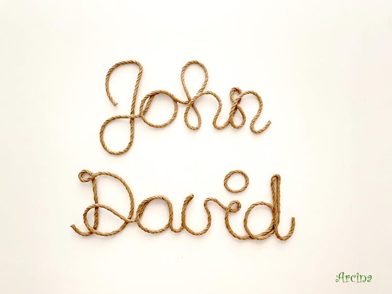 May include: The names John and David are written in cursive script using a single length of brown twisted rope. The letters are formed by the rope, creating a textured, three-dimensional appearance against a plain, light-colored background.