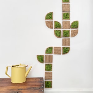 May include: A wall-mounted art installation composed of square and semi-circular frames wrapped in natural jute rope, alternating between empty rope-bound squares and squares filled with vibrant green preserved moss, arranged in a cactus shape.