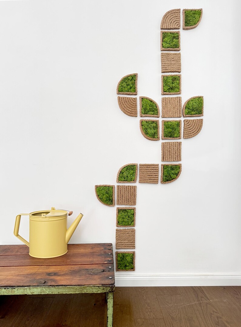 May include: A wall-mounted art installation composed of square and semi-circular frames wrapped in natural jute rope, alternating between empty rope-bound squares and squares filled with vibrant green preserved moss, arranged in a cactus shape.