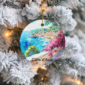 Peut inclure: Une d&eacute;coration en c&eacute;ramique ronde illustrant un paysage c&ocirc;tier de la C&ocirc;te d'Azur. L'image montre une mer bleue avec des voiliers, une ville &agrave; flanc de colline et des fleurs roses vives au premier plan. Le texte C&ocirc;te d'Azur est inscrit en bas.
