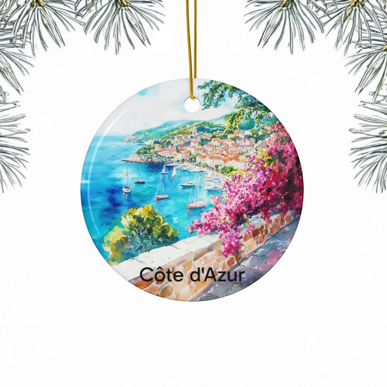 Peut inclure: Une d&eacute;coration en c&eacute;ramique ronde orn&eacute;e d'une peinture &agrave; l'aquarelle repr&eacute;sentant une ville c&ocirc;ti&egrave;re avec des voiliers sur une mer bleue, des fleurs de bougainvillier rose vif et un mur en pierre. Le texte C&ocirc;te d'Azur est imprim&eacute; en noir.