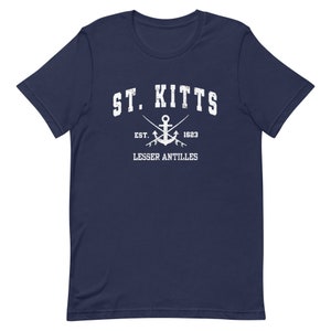 May include: A navy blue t-shirt with a white graphic design. The graphic features the text "ST. KITTS" in a vintage style font, an anchor with crossed oars, and the text "EST. 1623 LESSER ANTILLES".