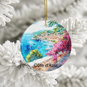 Peut inclure: Une d&eacute;coration en c&eacute;ramique ronde orn&eacute;e d'une peinture aquarelle vibrante de la c&ocirc;te d'Azur, avec des eaux bleues, des voiliers, un village &agrave; flanc de colline et des fleurs de bougainvilliers rose vif. Le texte C&ocirc;te d'Azur est inscrit en bas.