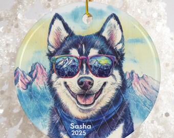 May include: Round ceramic ornament featuring a smiling husky wearing sunglasses with a mountain reflection. The dog has a blue bandana and the text "Sasha 2025". The ornament has a gold string for hanging.