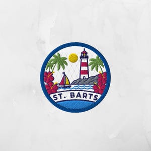 May include: A circular embroidered patch featuring a red and white lighthouse, a yellow sun, green palm trees, a sailboat, and red hibiscus flowers. The text ST. BARTS is embroidered in dark blue at the bottom against a white background.
