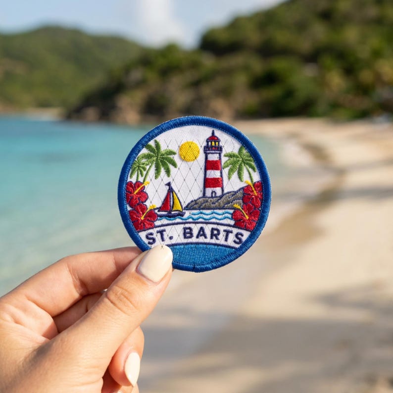 May include: A circular embroidered patch featuring a red and white lighthouse, a sailboat, palm trees, and red hibiscus flowers against a white background. The text ST. BARTS is stitched in blue at the bottom, all enclosed by a blue border.