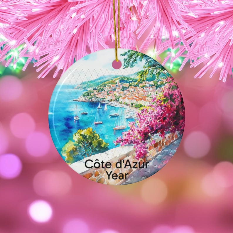 Peut inclure: Une d&eacute;coration en c&eacute;ramique ronde orn&eacute;e d'une peinture &agrave; l'aquarelle repr&eacute;sentant une ville c&ocirc;ti&egrave;re m&eacute;diterran&eacute;enne avec des voiliers sur l'eau bleue, des fleurs de bougainvillier rose vif et un mur en pierre. Le texte C&ocirc;te d'Azur Year est imprim&eacute; en bas.