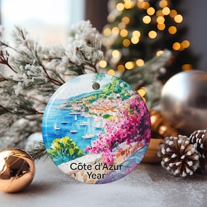 Peut inclure: Une d&eacute;coration ronde en c&eacute;ramique repr&eacute;sentant une sc&egrave;ne c&ocirc;ti&egrave;re peinte de la C&ocirc;te d'Azur avec de l'eau bleue, des voiliers et des fleurs roses. Le texte "C&ocirc;te d'Azur Year" est imprim&eacute; en noir au bas de la surface circulaire.