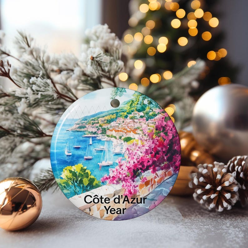 Peut inclure: Une d&eacute;coration ronde en c&eacute;ramique repr&eacute;sentant une sc&egrave;ne c&ocirc;ti&egrave;re peinte de la C&ocirc;te d'Azur avec de l'eau bleue, des voiliers et des fleurs roses. Le texte "C&ocirc;te d'Azur Year" est imprim&eacute; en noir au bas de la surface circulaire.