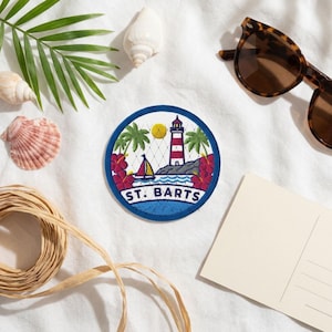 May include: A circular embroidered patch featuring a red and white lighthouse, a sailboat, palm trees, and red hibiscus flowers. The text ST. BARTS is embroidered in blue at the bottom of the patch, which has a dark blue border.