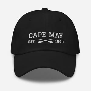 May include: Black baseball cap with white embroidered text reading "CAPE MAY EST. 1848" and crossed oars. The cap features a curved peak and a fabric strap.