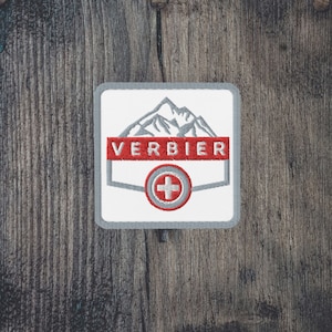 May include: A white embroidered patch with a gray mountain range, the word "VERBIER" in red, and a red Swiss cross in a white circle.