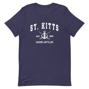 May include: A navy blue t-shirt with a white distressed graphic of the text "ST. KITTS" with an anchor and crossed fishing poles underneath. The text "EST. 1623" and "LESSER ANTILLES" are also included in the graphic.